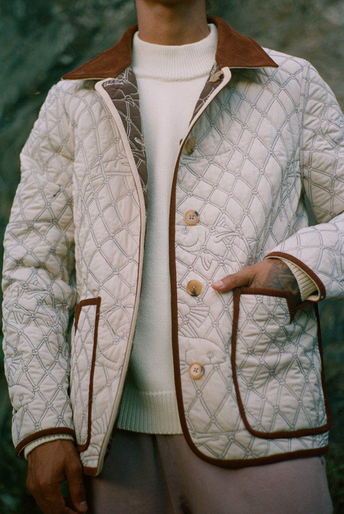A person wearing a cream quilted jacket with brown trim over a white turtleneck sweater.