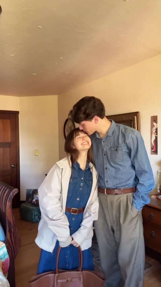 A young couple posing together, the woman wearing a denim dress and white jacket.