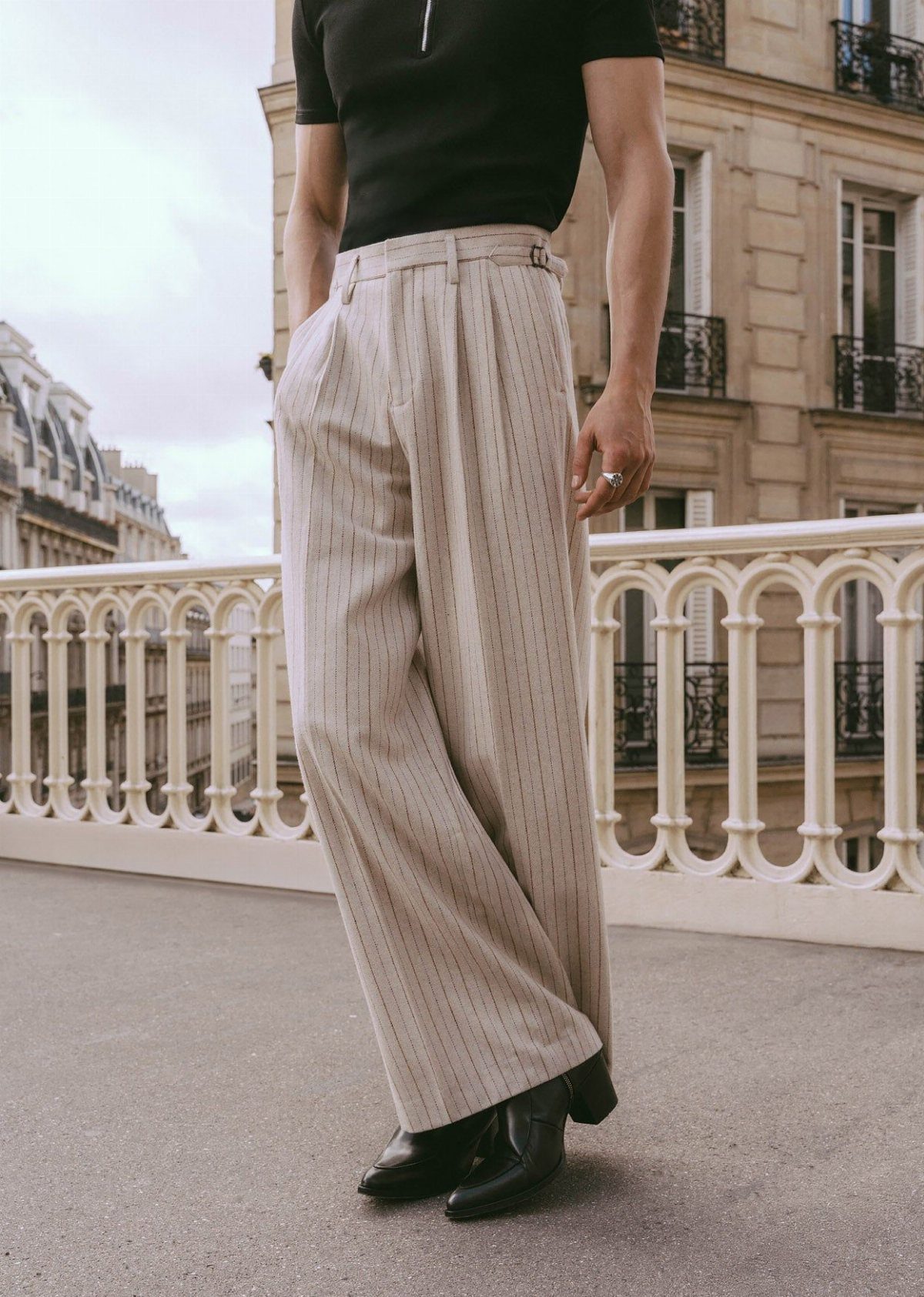 A person wearing high-waisted wide leg striped trousers and a black shirt outdoors.