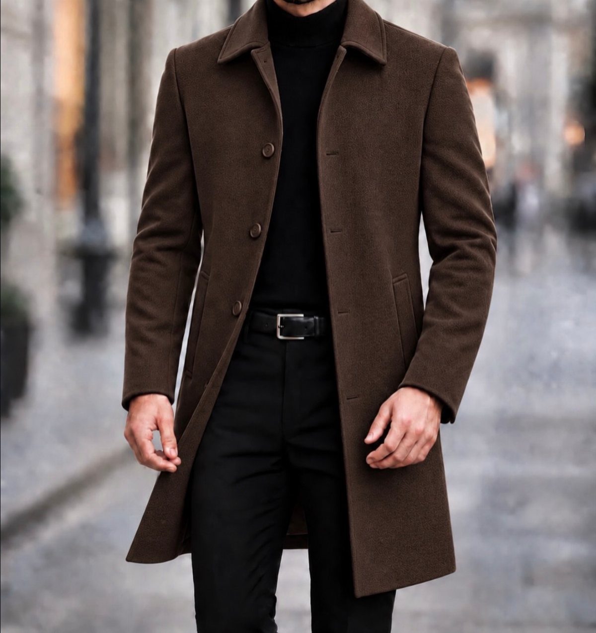 A person wearing a long brown wool coat and black clothing on a city street.