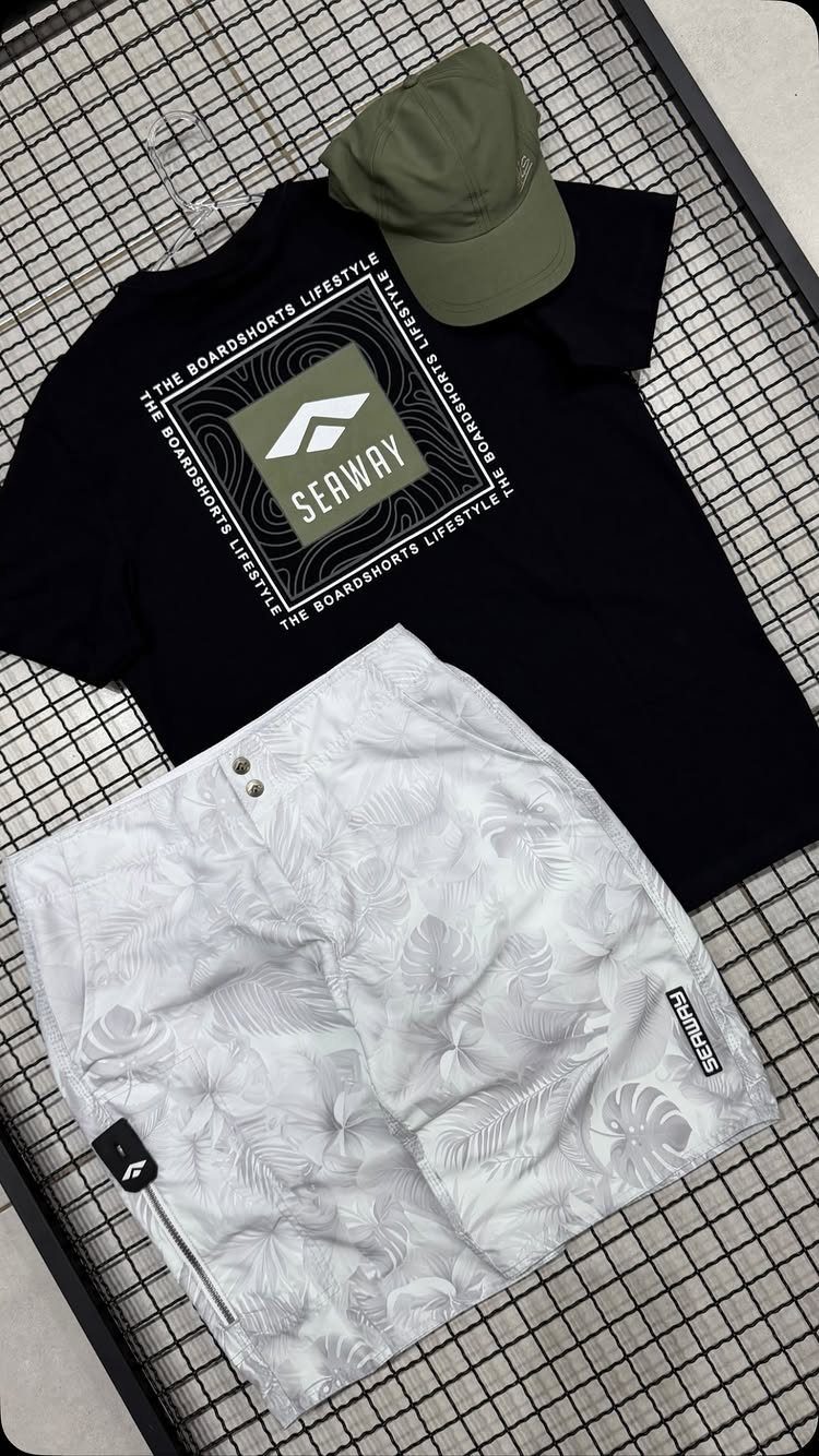 Black t-shirt, patterned swim shorts, and an olive green cap arranged on a wire grid.