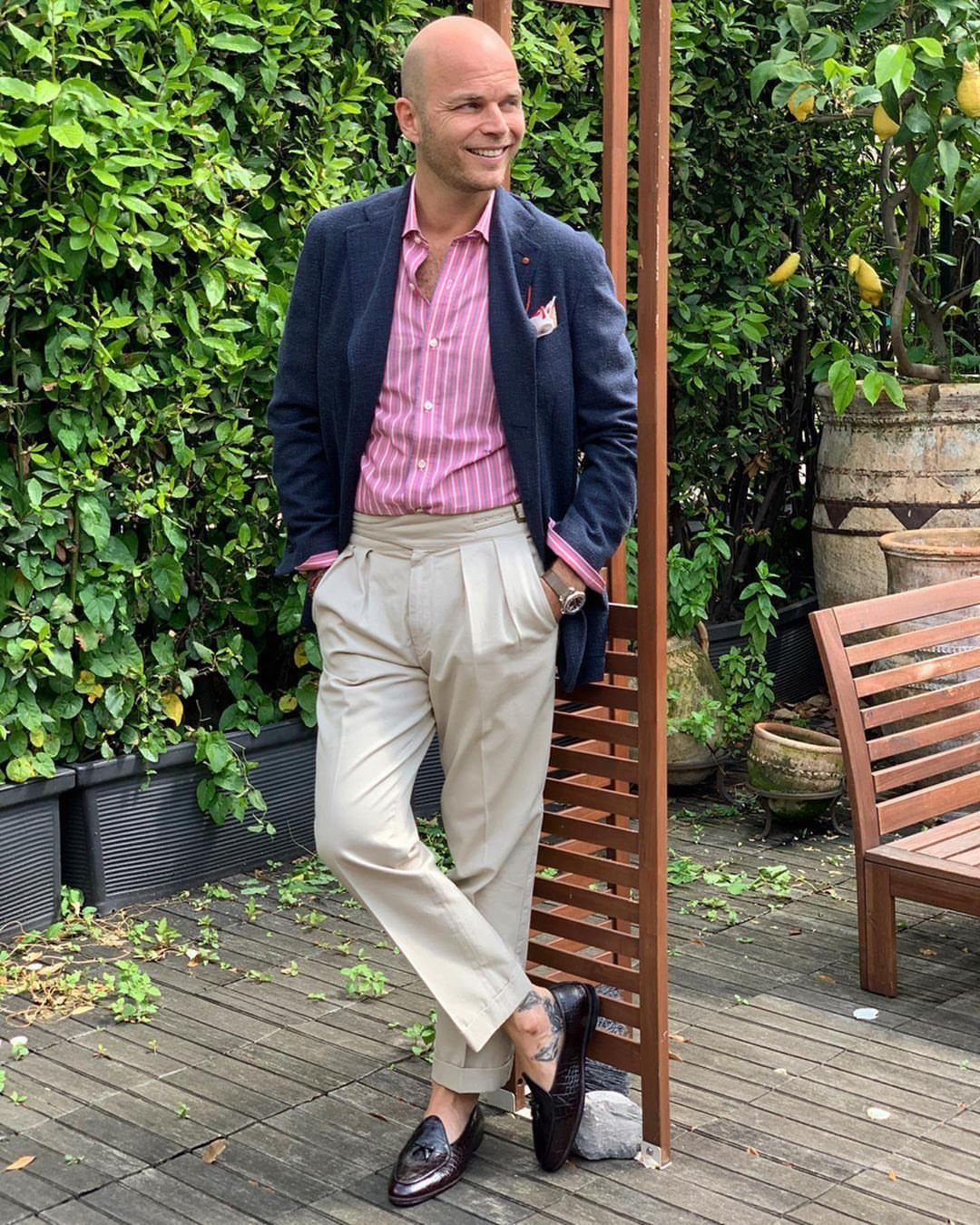 A man wearing a navy blue blazer and pink striped shirt with cream pants.