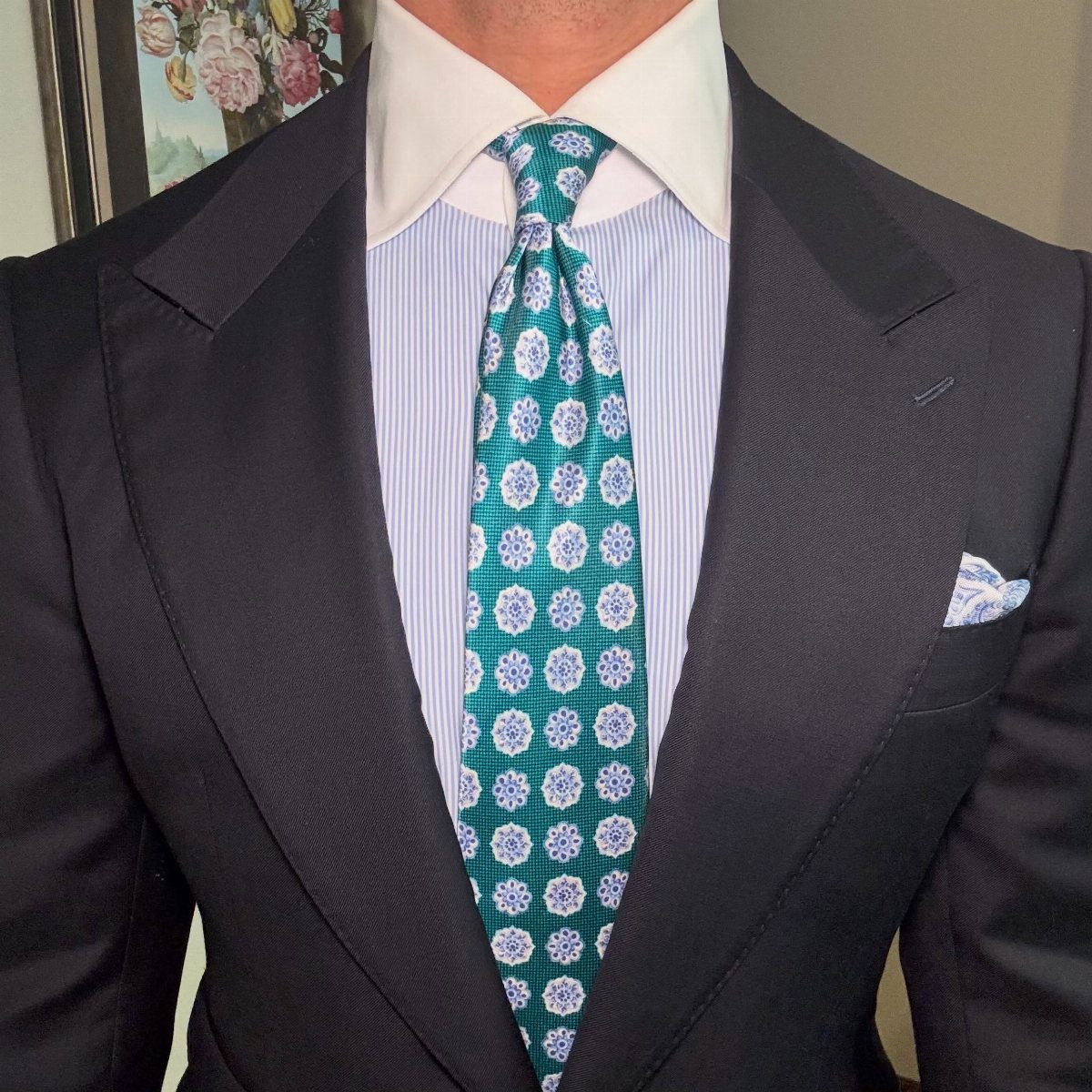Man wearing a dark navy suit with a light blue striped shirt and teal tie.