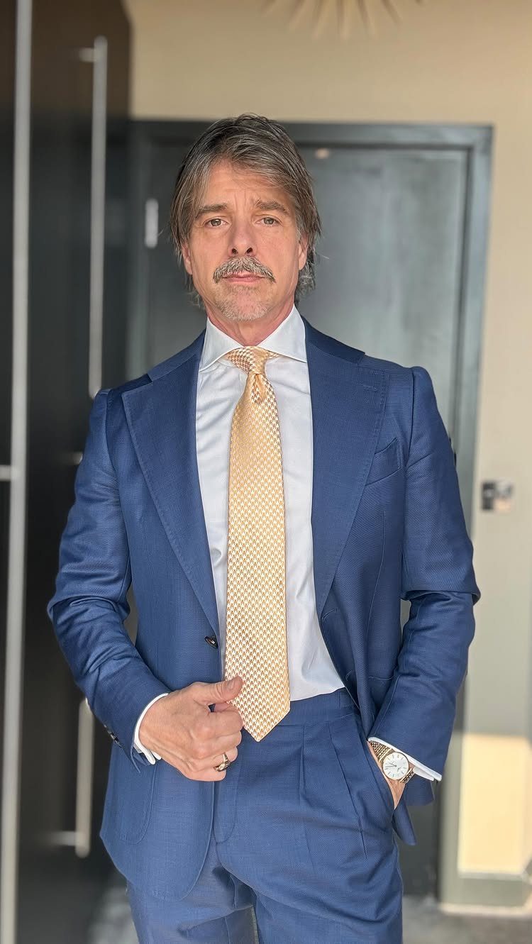 Man wearing a blue suit with a white shirt and gold patterned tie.