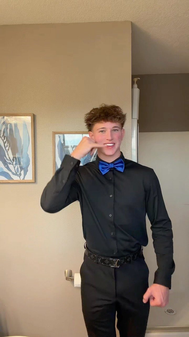 A young man smiling while wearing a black shirt and a vibrant blue bow tie.