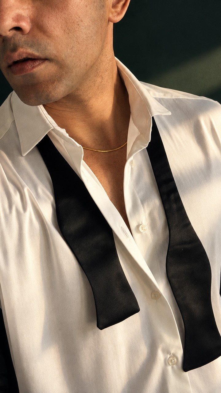Man wearing an unbuttoned white shirt with a black bow tie draped loosely around his neck.