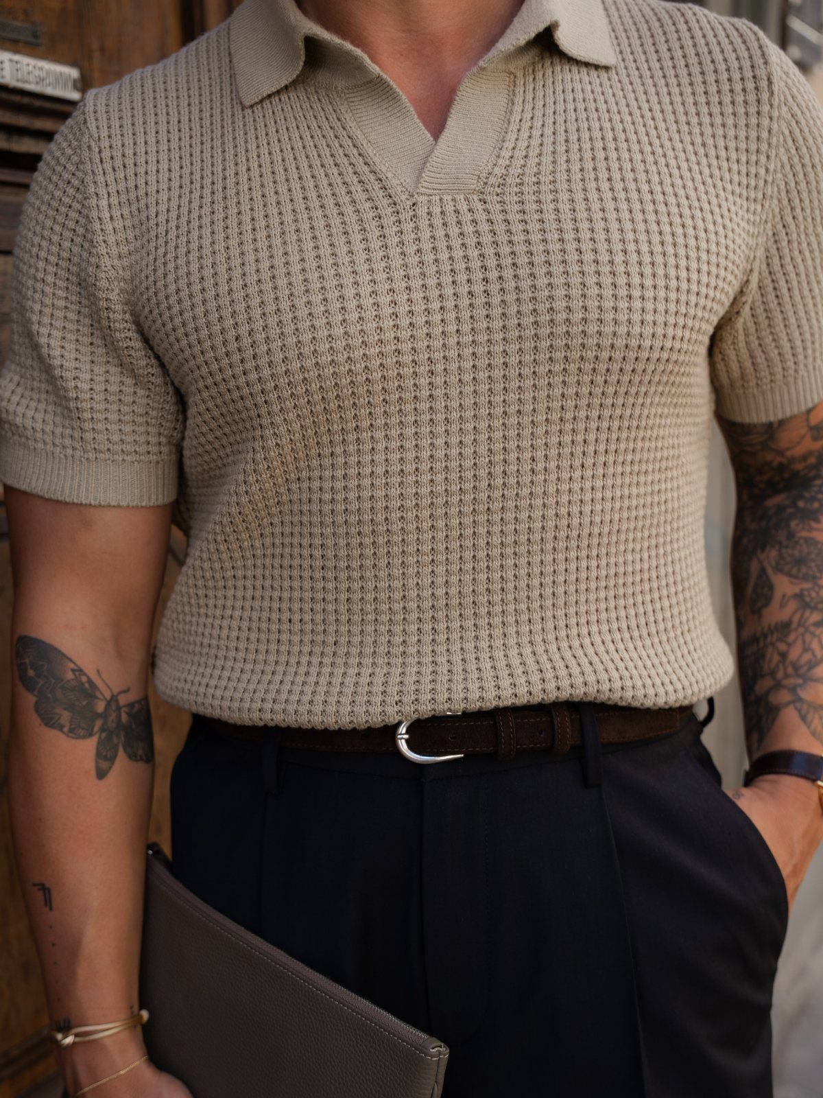 Man wearing a beige knit polo shirt tucked into dark tailored trousers with a brown belt.