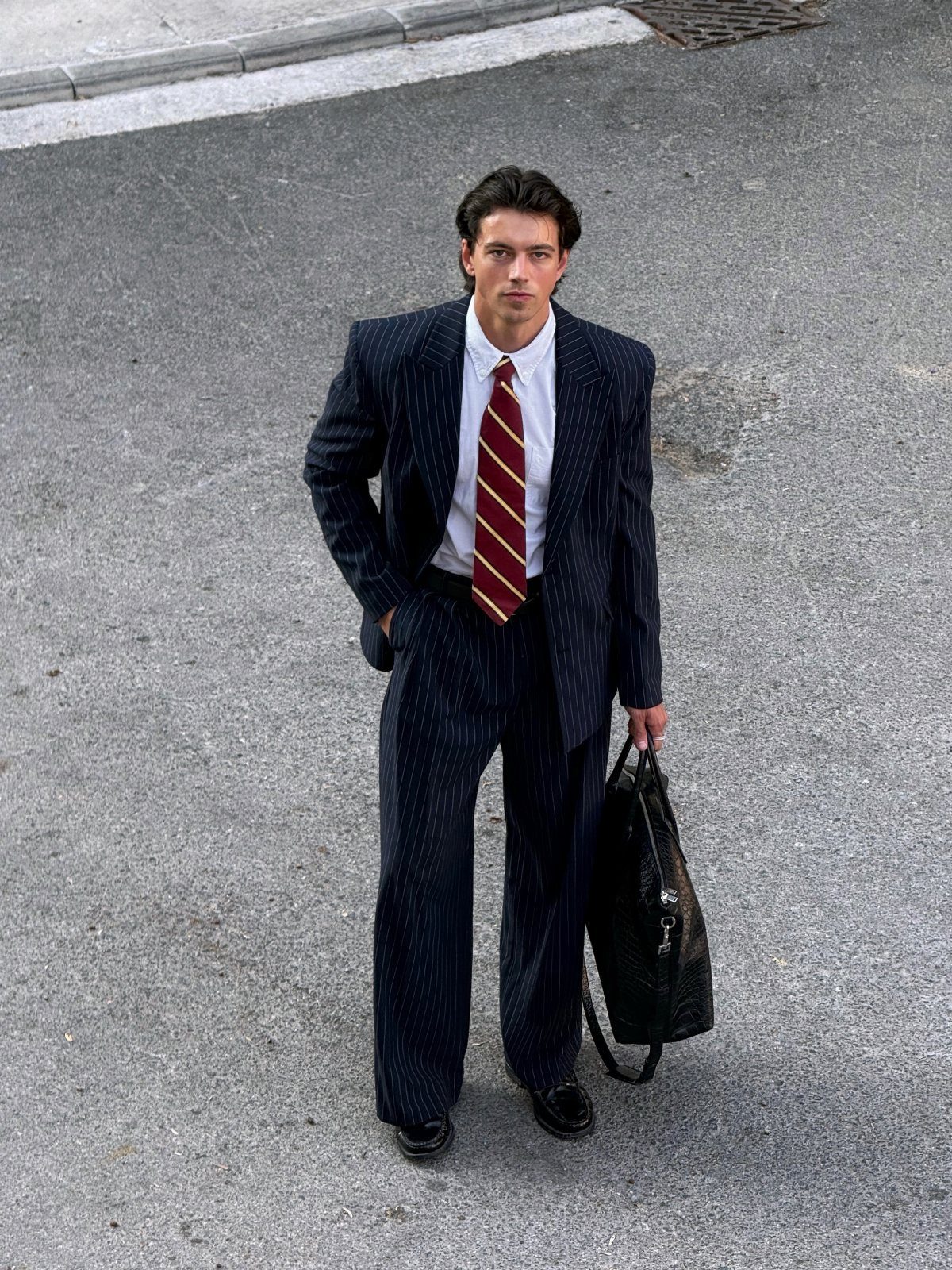 A man in a navy pinstripe suit and striped tie standing on an asphalt street.