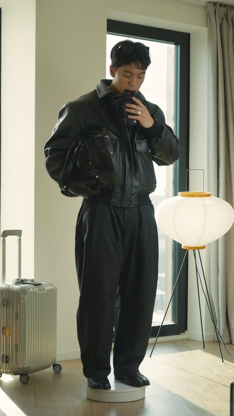 Man in an all-black outfit including a leather jacket standing in a bright room.