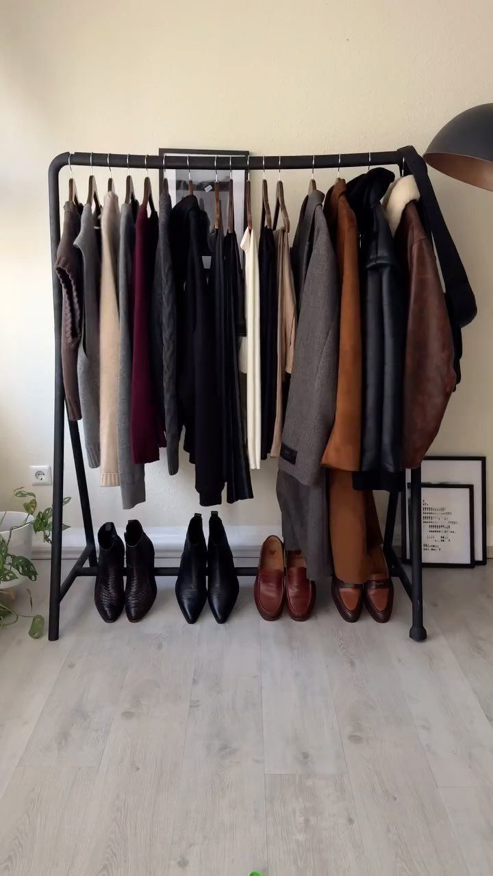 Various neutral colored clothes hanging on a black rack with leather shoes underneath.