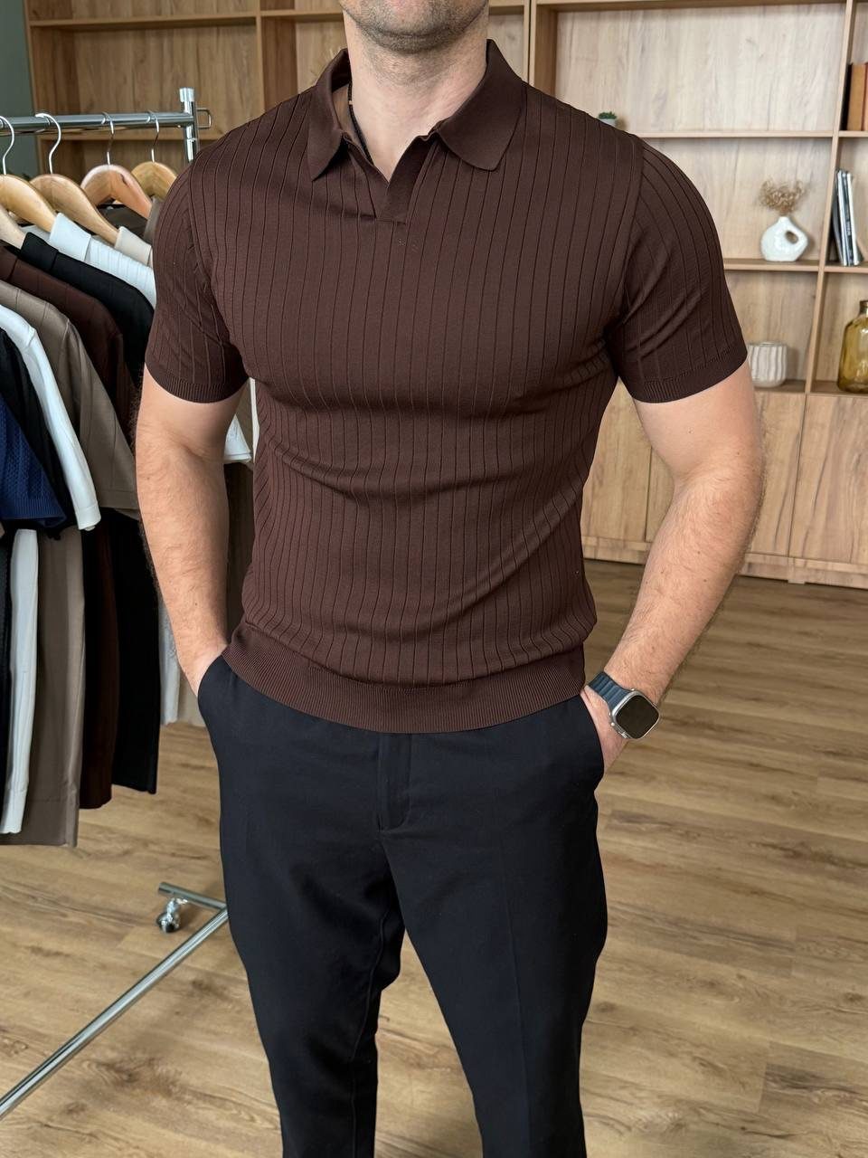 Man wearing a brown ribbed knit polo shirt and black trousers standing in a clothing store.