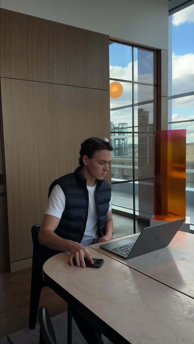 A man wearing a navy quilted vest works on a laptop at a desk.