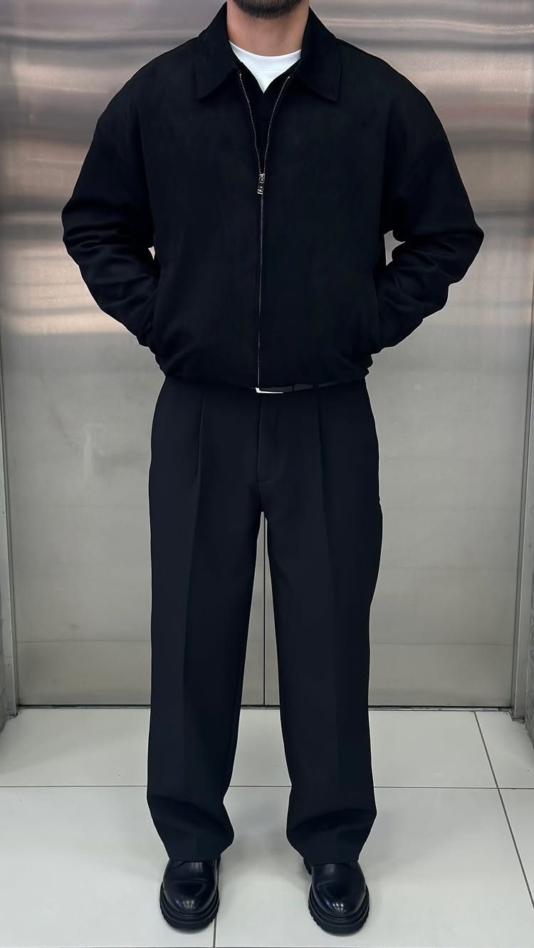 Man wearing a black collared jacket, black trousers, and black leather shoes.