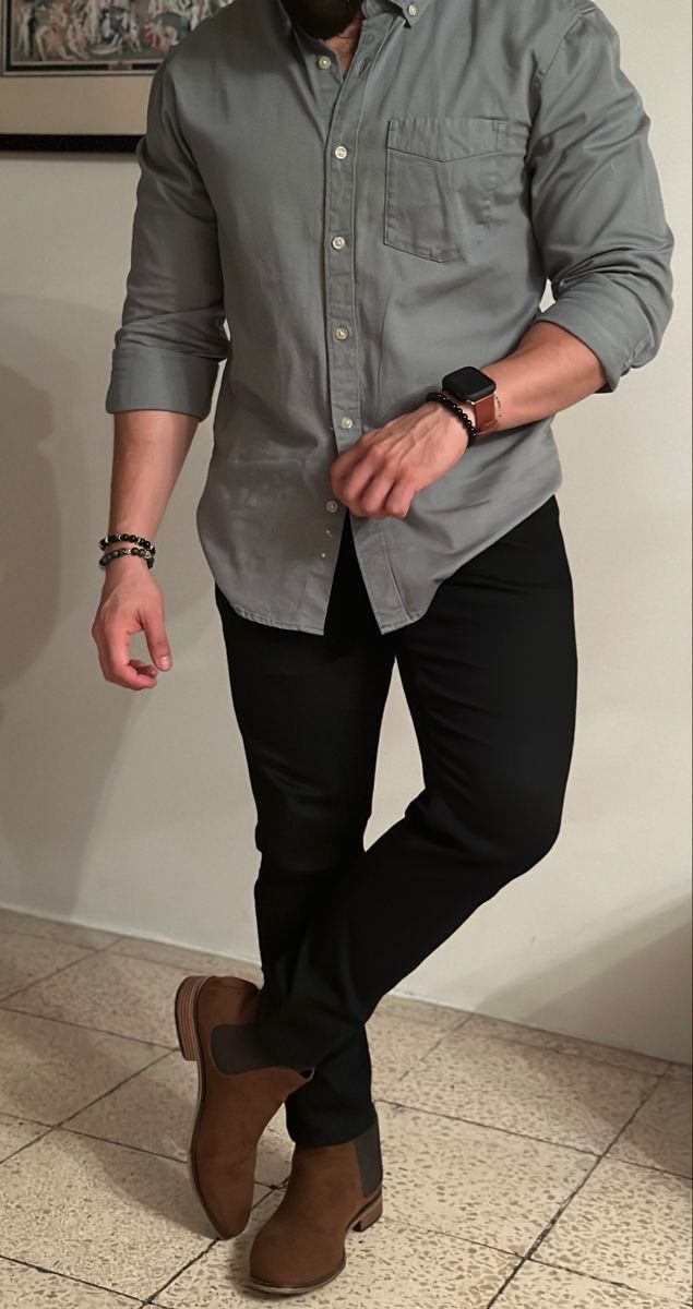 Man wearing a grey button-down shirt, black pants, and brown suede Chelsea boots.