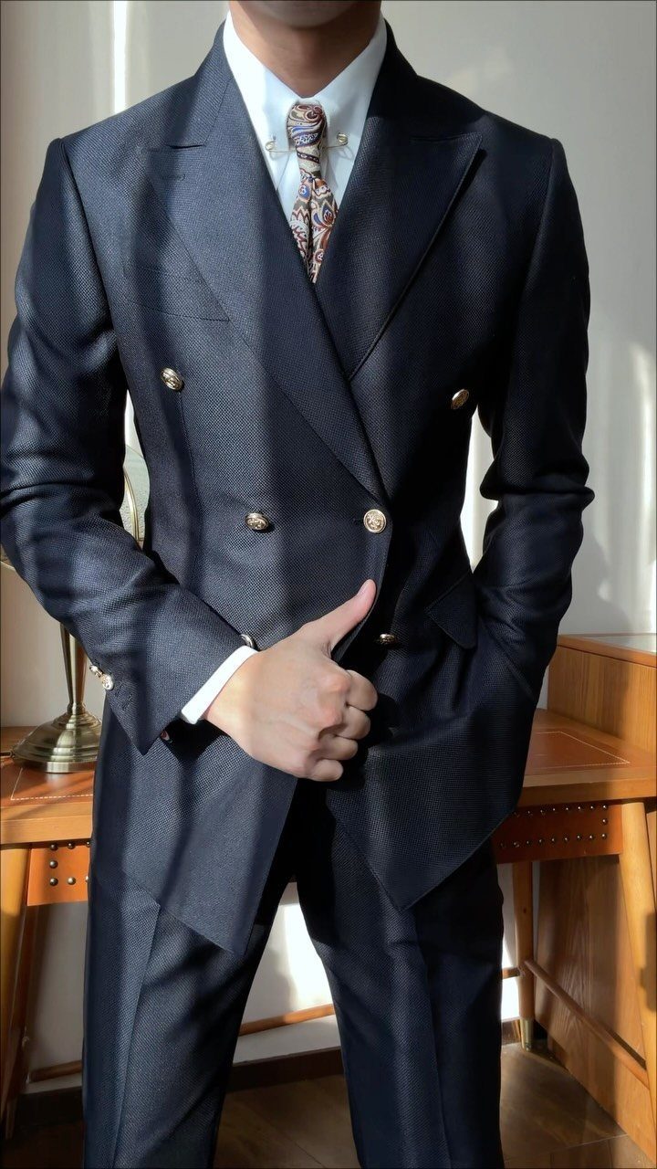 Man wearing a navy blue double-breasted suit with gold buttons and a patterned tie.