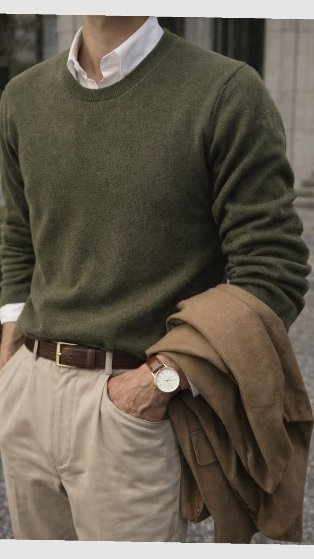 Man wearing an olive green crewneck sweater, white shirt, and tan trousers with a brown belt.