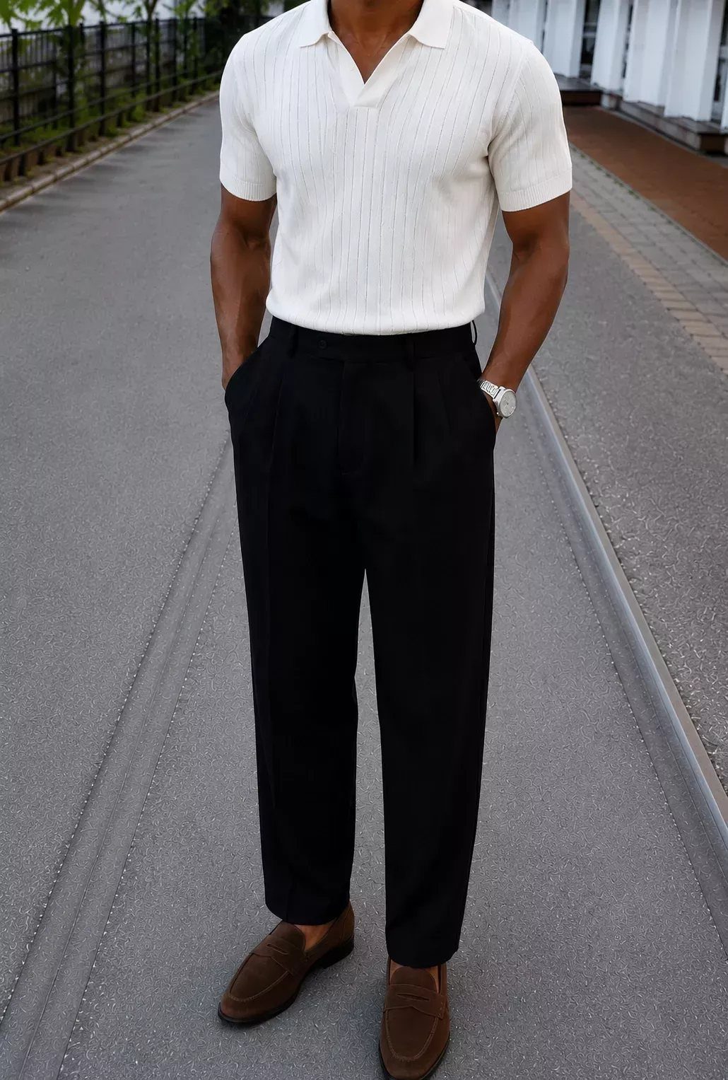 Man wearing a white polo shirt, black trousers, and brown loafers standing on a path.