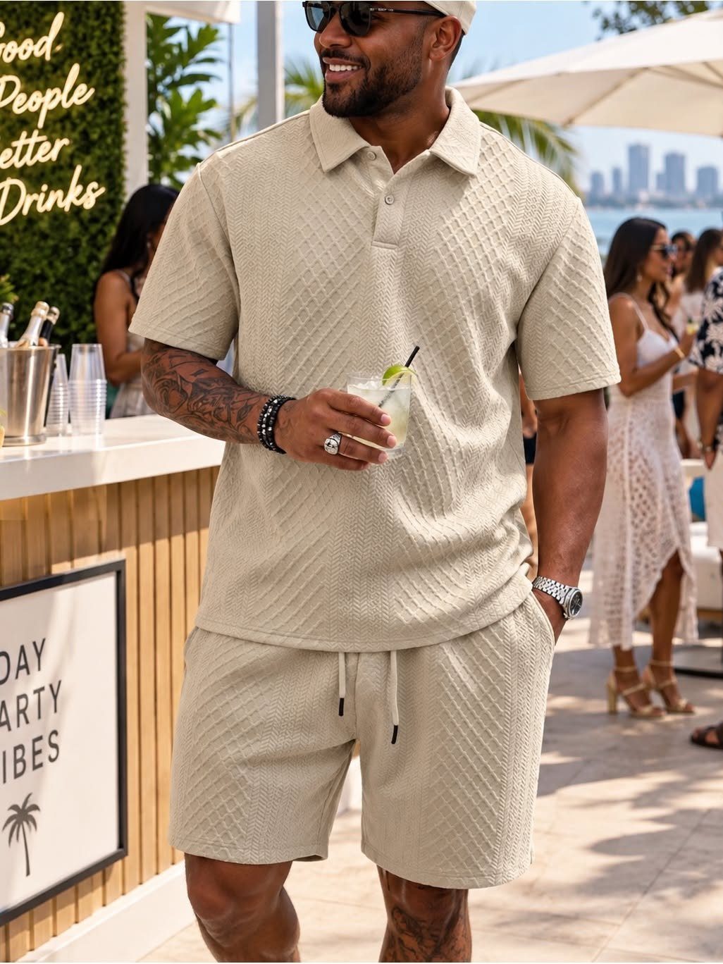 A man in a beige textured polo shirt and matching shorts holding a cocktail outdoors.