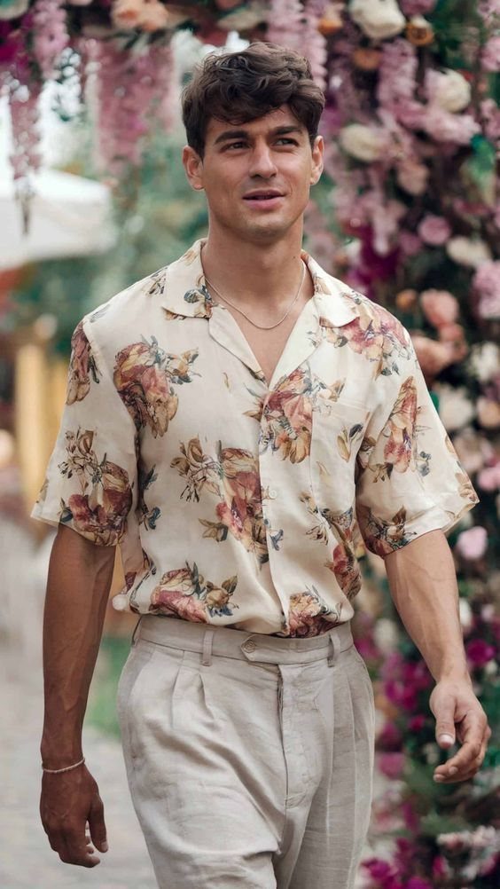 Man wearing a floral print summer shirt and beige linen trousers walking through a garden.