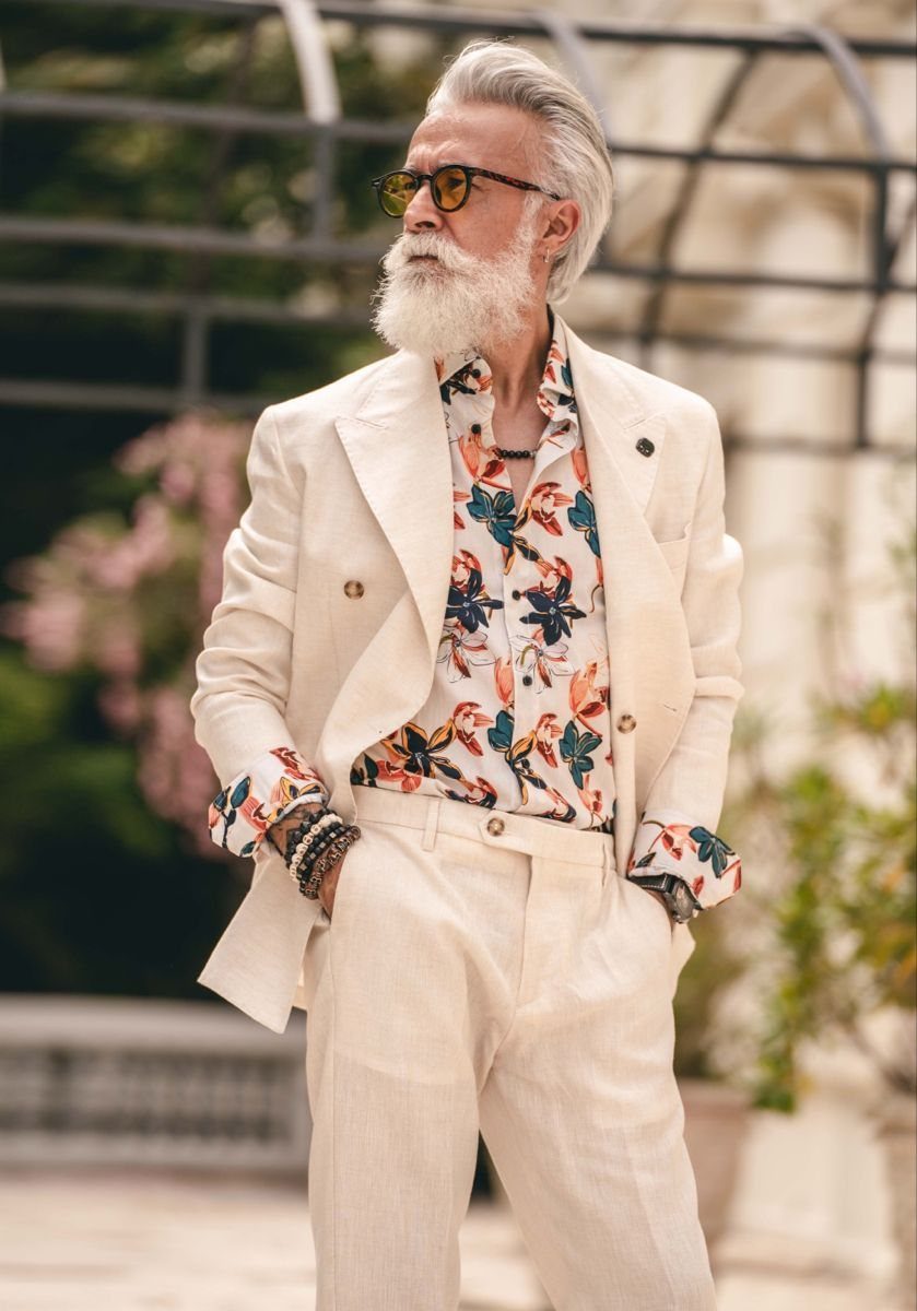 Older man with a white beard wearing a white linen suit and floral shirt.