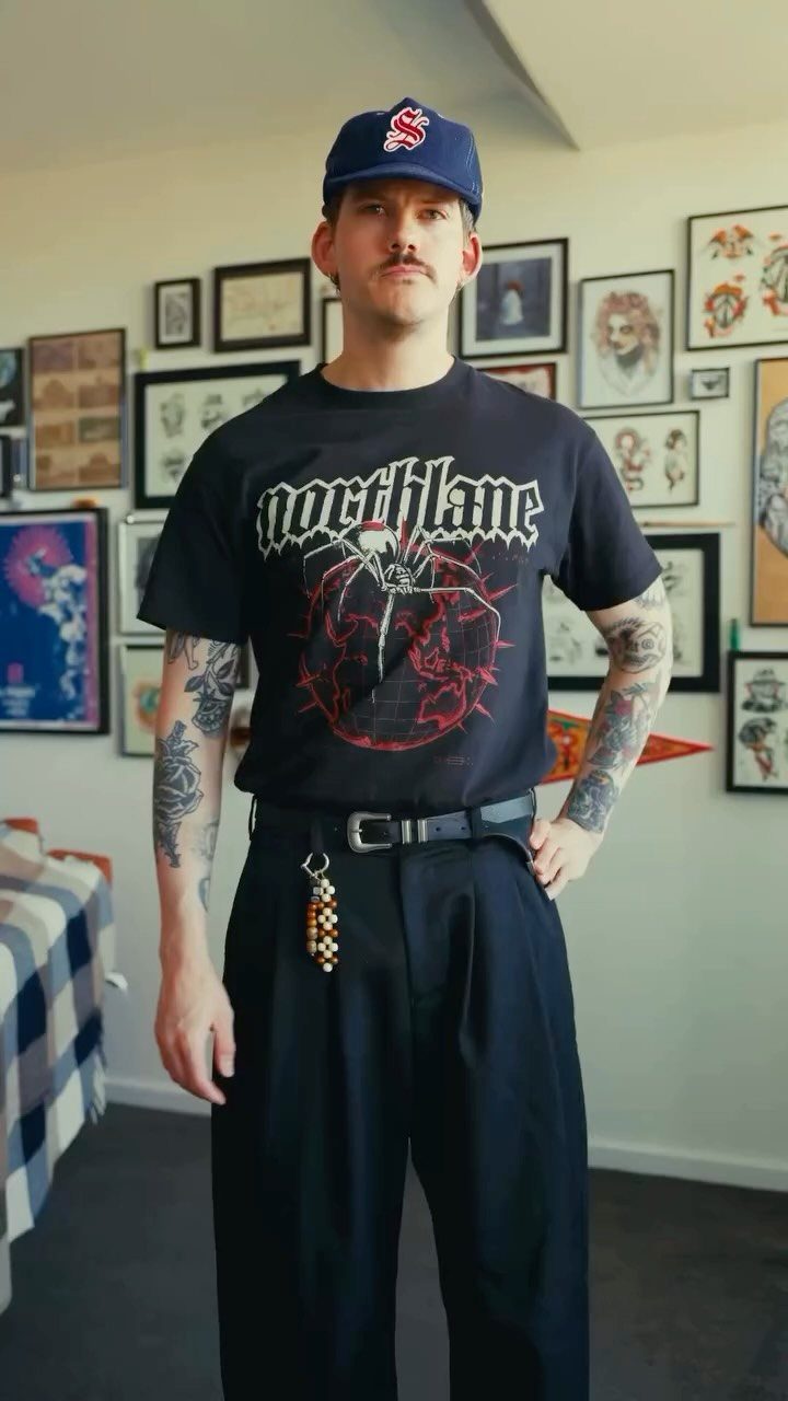 Man in a black Northlane band t-shirt and black trousers standing in a room.