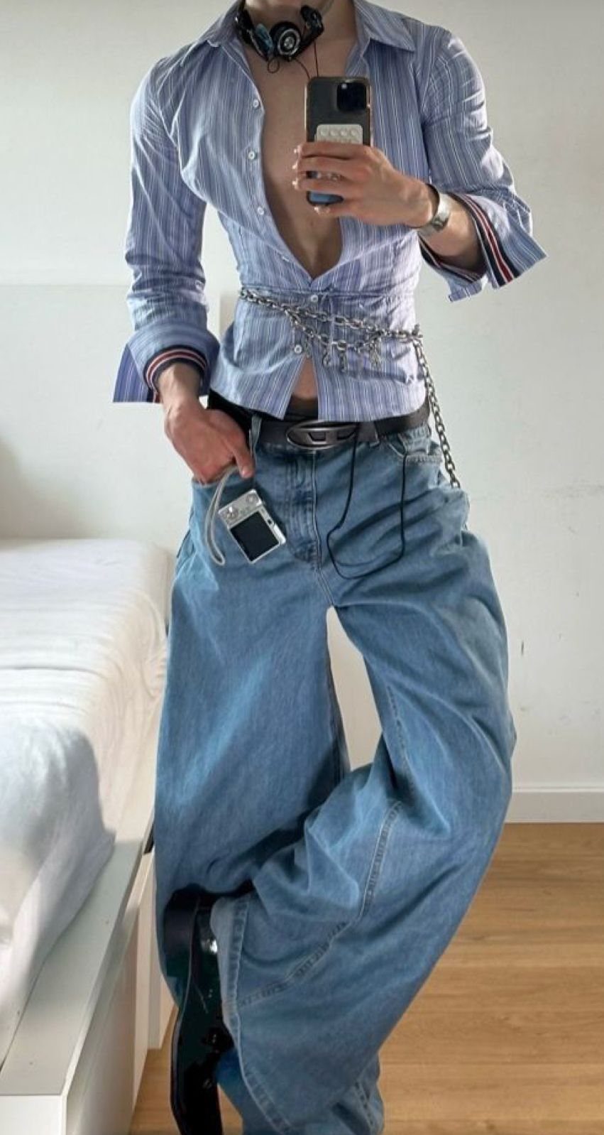Person in a striped shirt with a chain belt and baggy blue denim jeans.