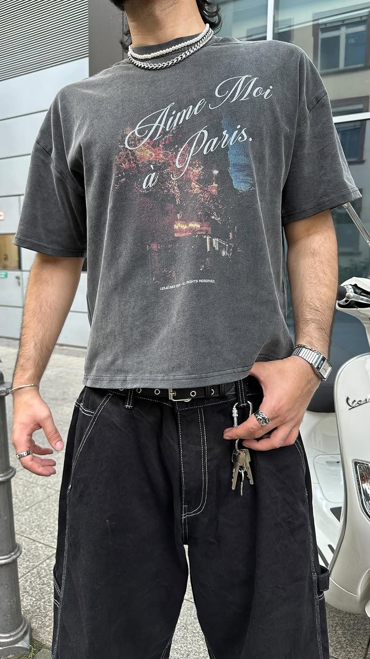 Person wearing a charcoal graphic t-shirt and black baggy trousers with a silver chain necklace.