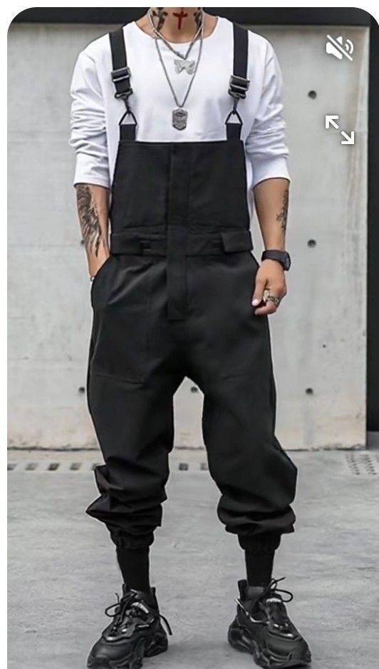 A person wearing black overalls over a white long-sleeved shirt with chunky black sneakers.