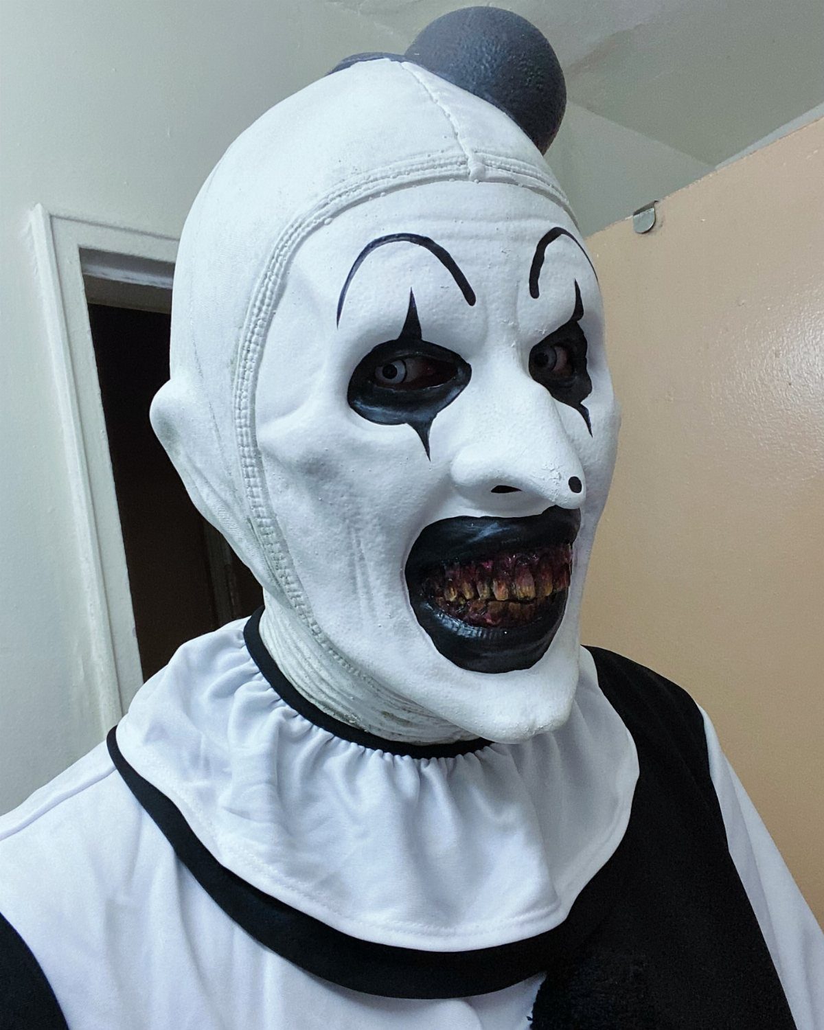 A person wearing a creepy white clown mask with black eye details and a toothy grin.