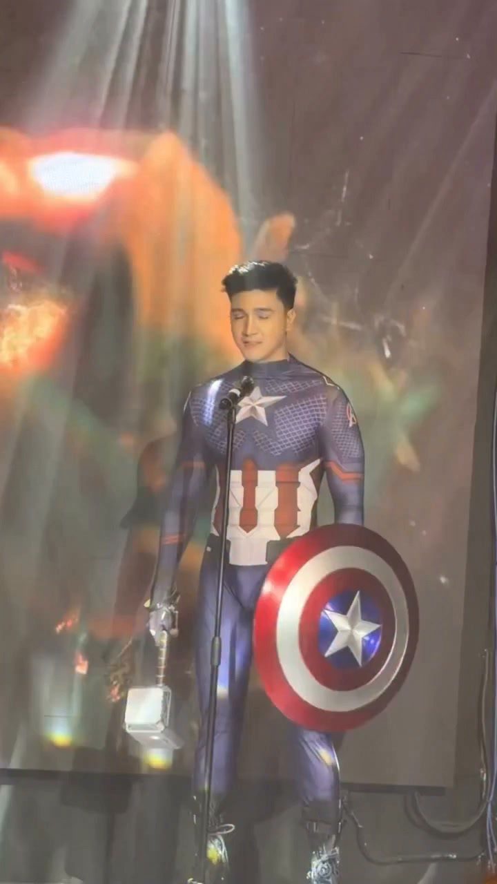 A man in a Captain America superhero costume holding a shield on a stage.