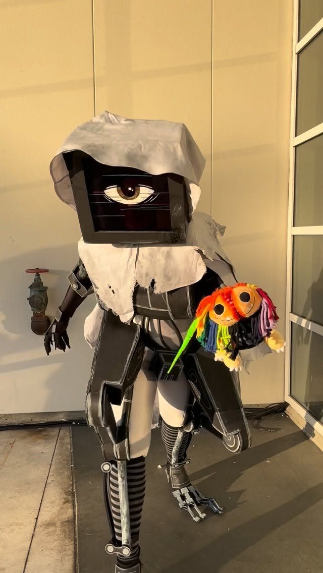 Person in a DIY mechanical costume with a large eye-patterned box head and tattered white fabric.