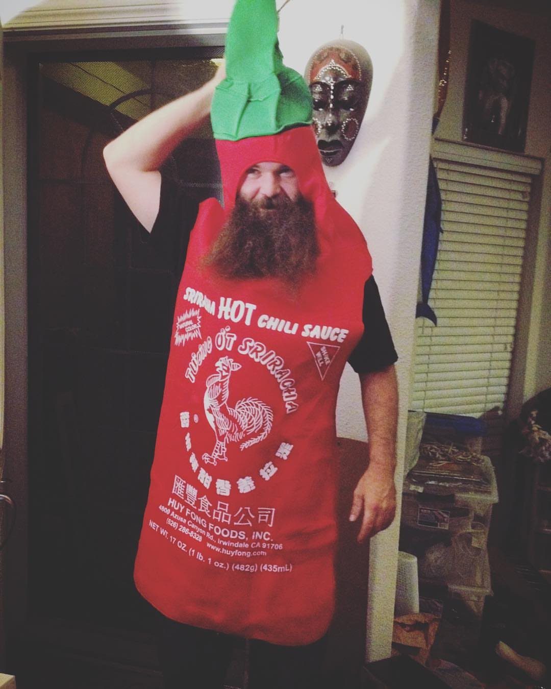A man with a thick beard wearing a red Sriracha hot chili sauce bottle costume.