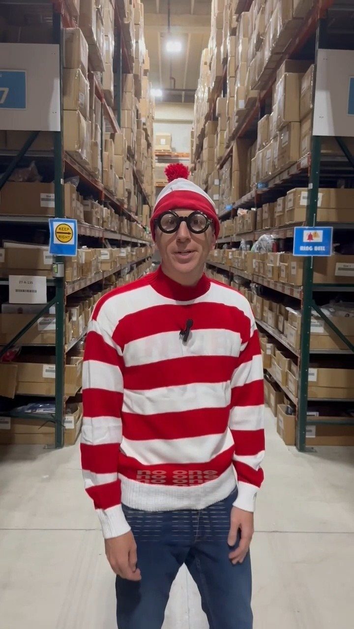 Man wearing a red and white striped sweater, matching beanie, and round glasses in a warehouse.