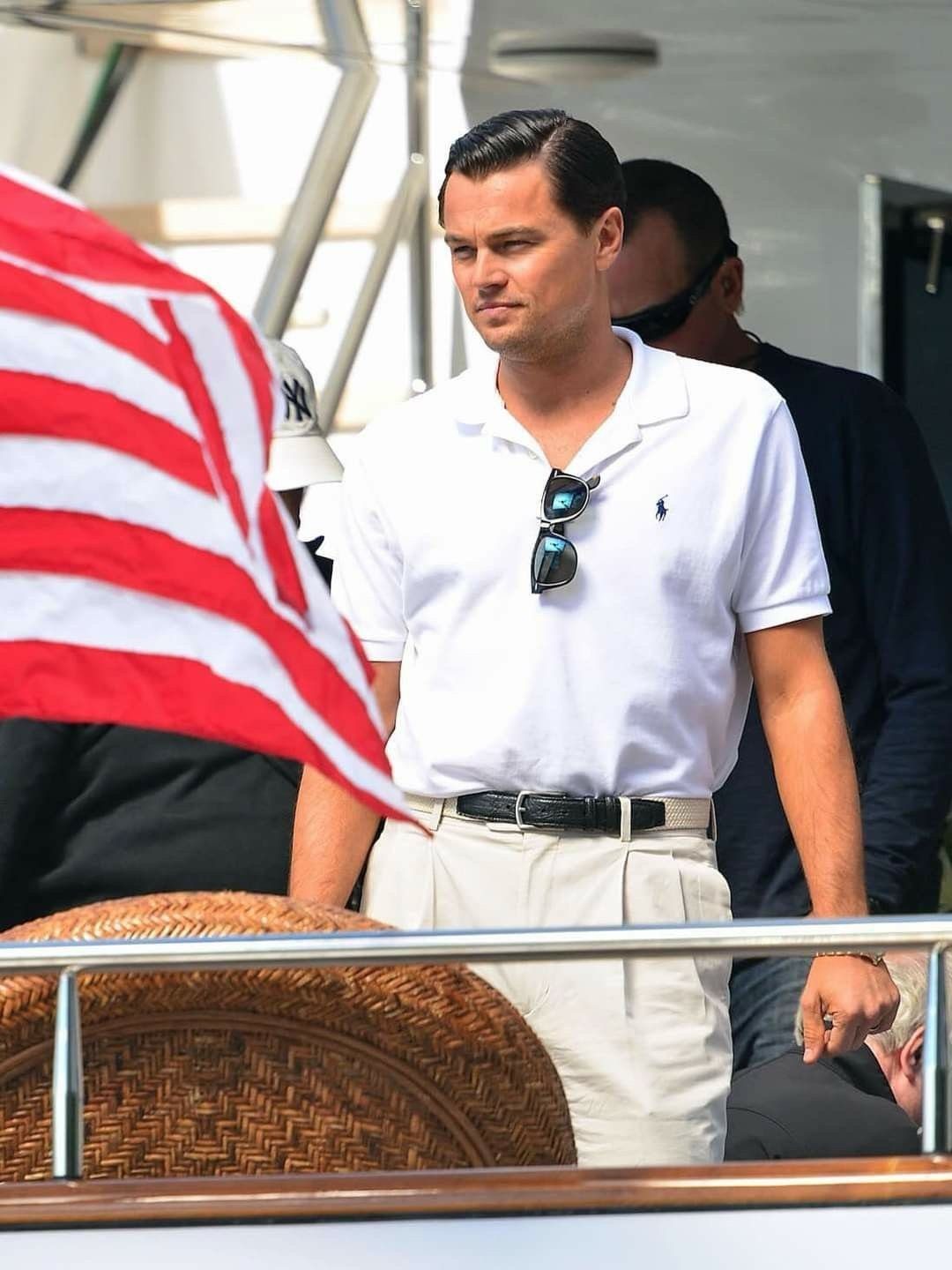 A man in a white polo shirt and light trousers standing near an American flag.