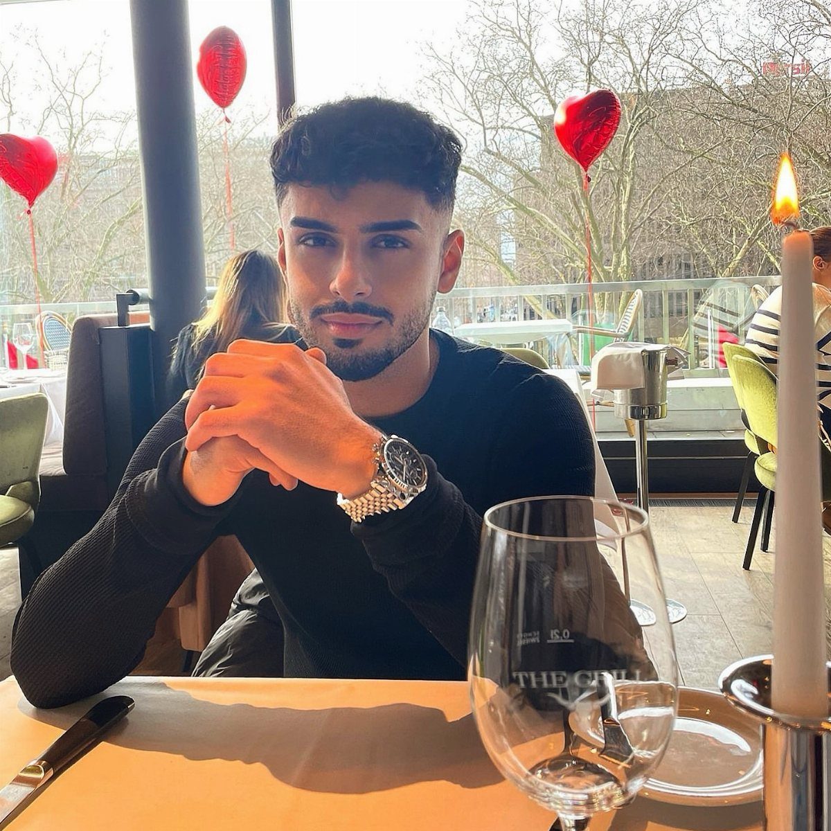 A young man with styled hair and a neat beard sitting at a restaurant table.