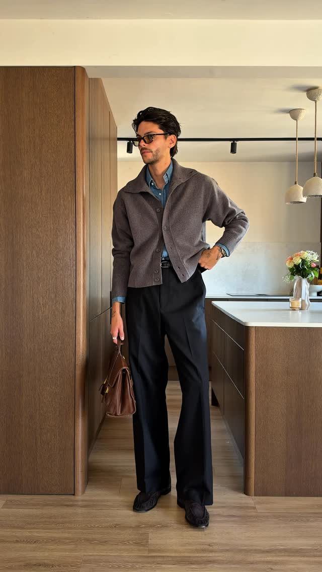 Man wearing a grey fine-knit cardigan over a blue collared shirt and dark trousers.