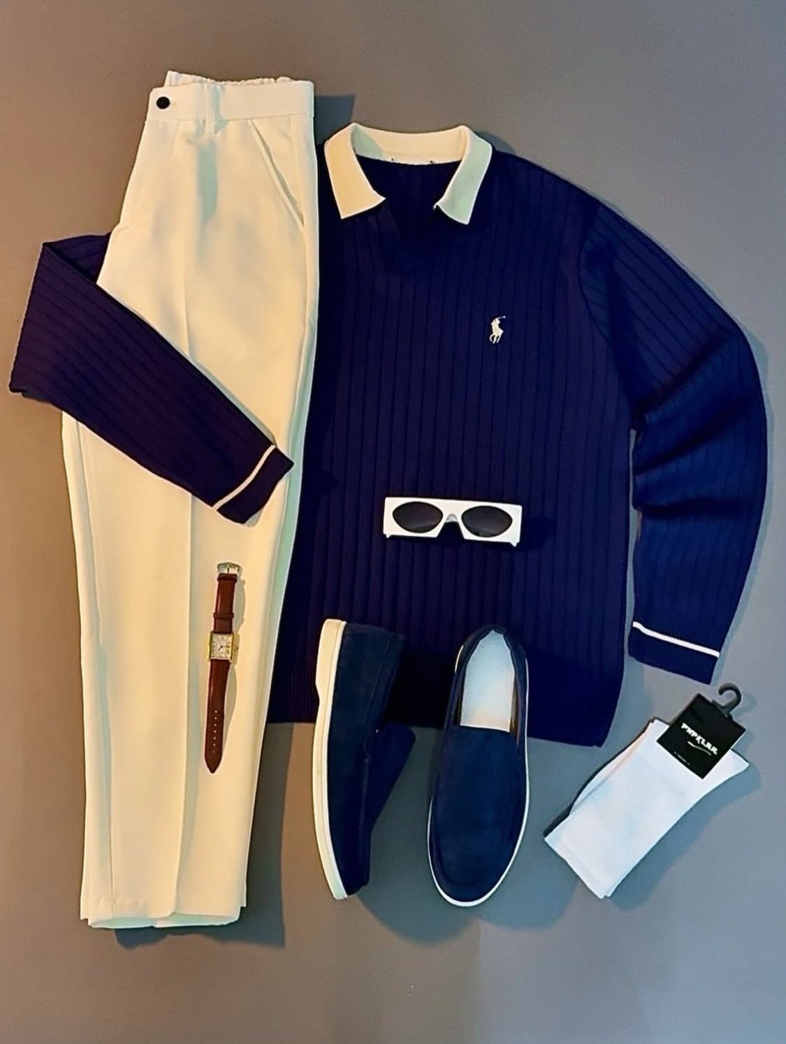 Navy blue ribbed polo, white trousers, blue loafers, and accessories arranged in a flat lay.