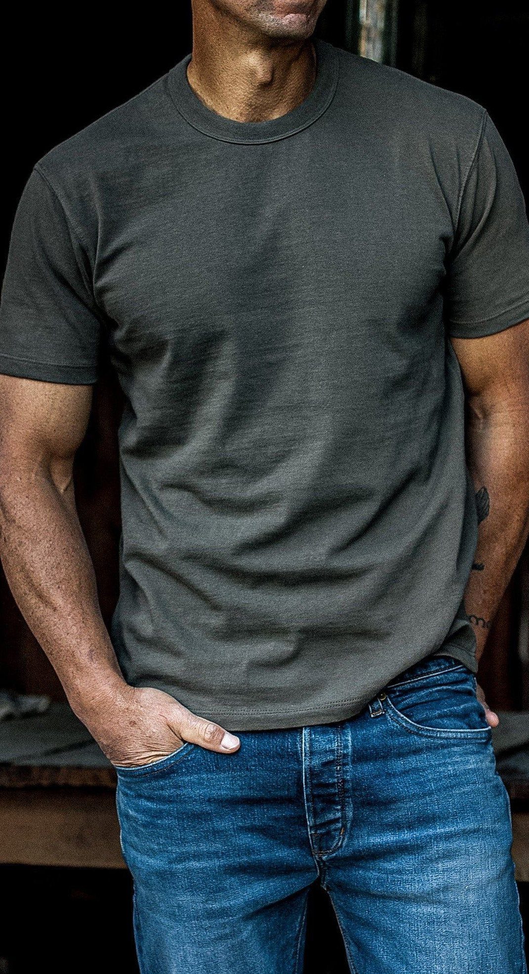 Man wearing a charcoal grey crewneck t-shirt and blue denim jeans.