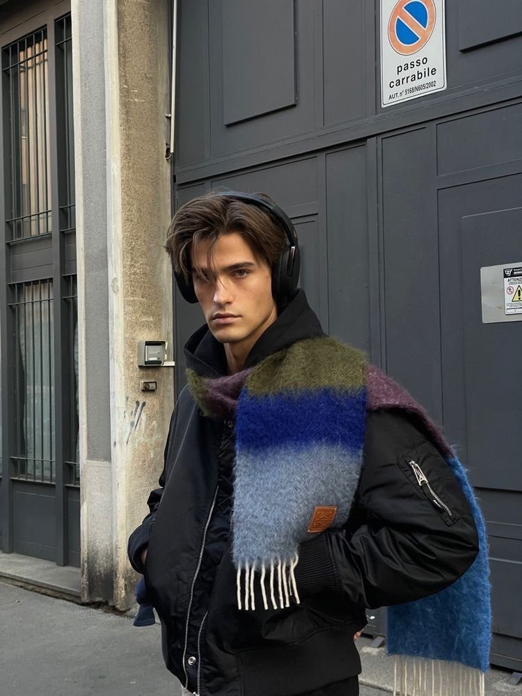 Young man wearing a black jacket and a colorful striped scarf with white fringe.