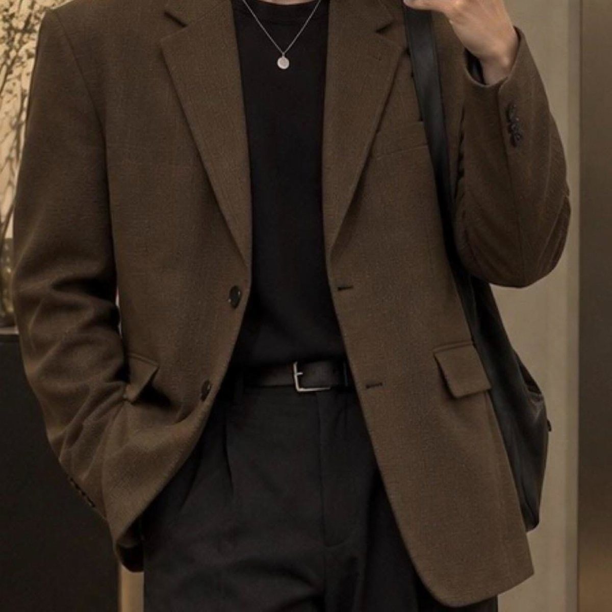 A person wearing a brown textured blazer over a black shirt and black trousers.