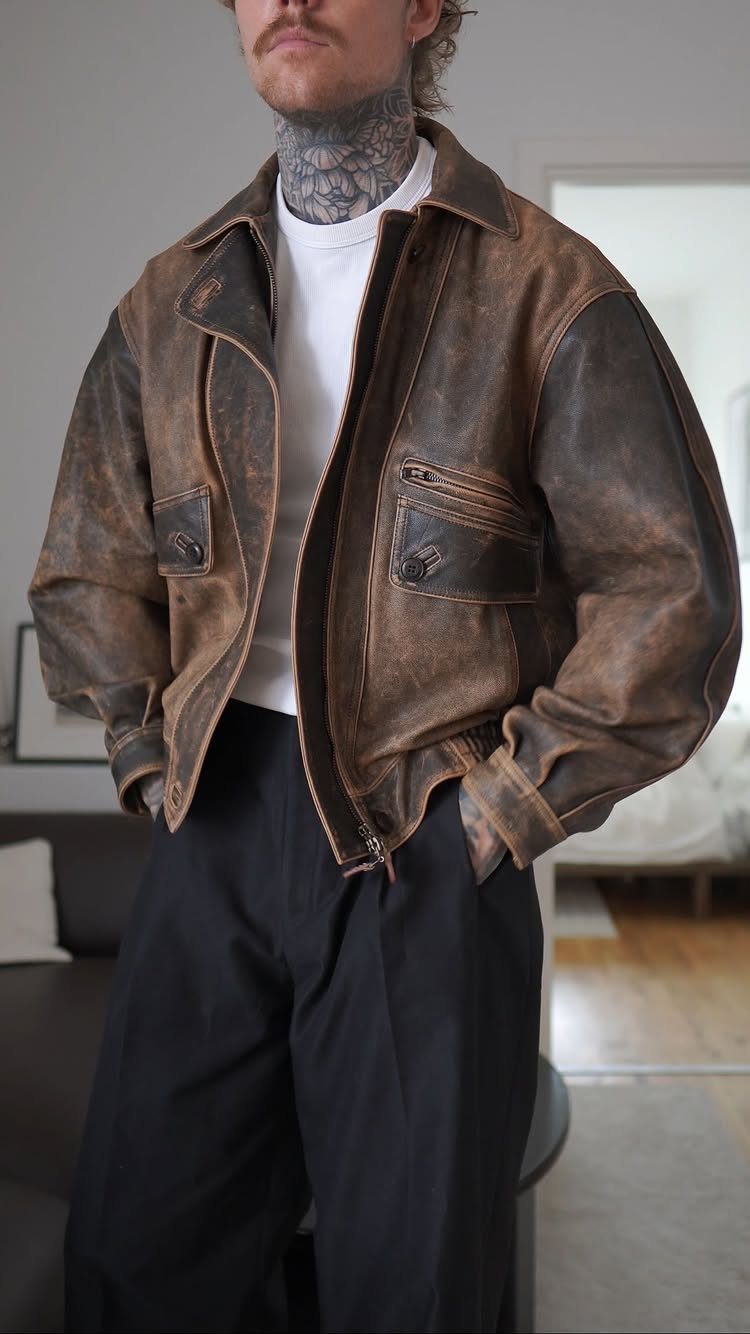 A man wearing a distressed brown leather jacket with a white t-shirt and black pants.