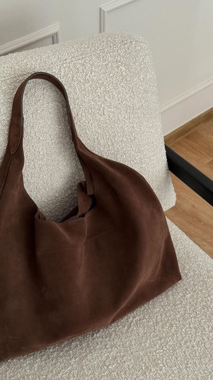 A large brown suede hobo bag resting on a light beige textured chair.
