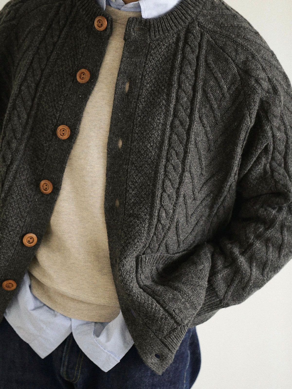 A person wearing a dark grey cable-knit cardigan over a beige sweater and blue shirt.