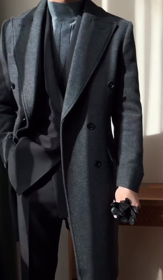A person wearing a long charcoal wool coat, a black blazer, and a blue turtleneck.