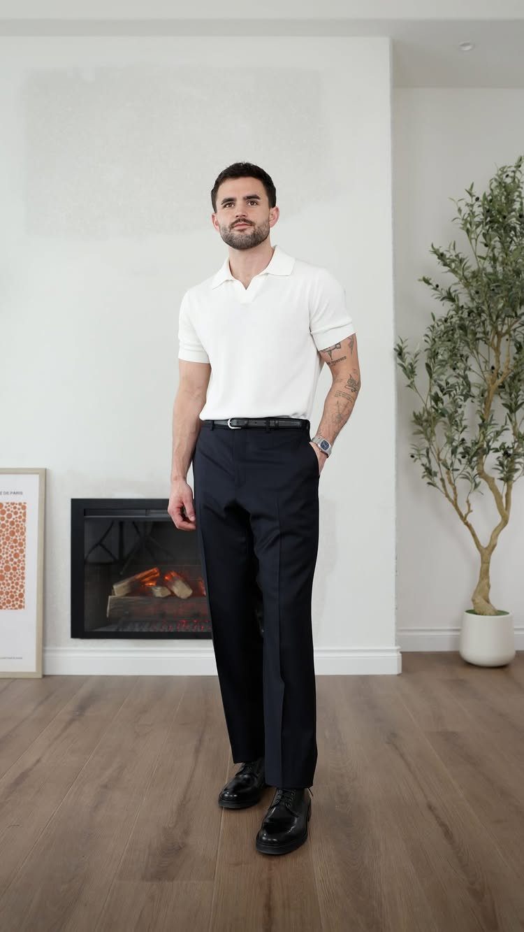 A man posing in a white polo shirt, dark trousers, and black dress shoes.