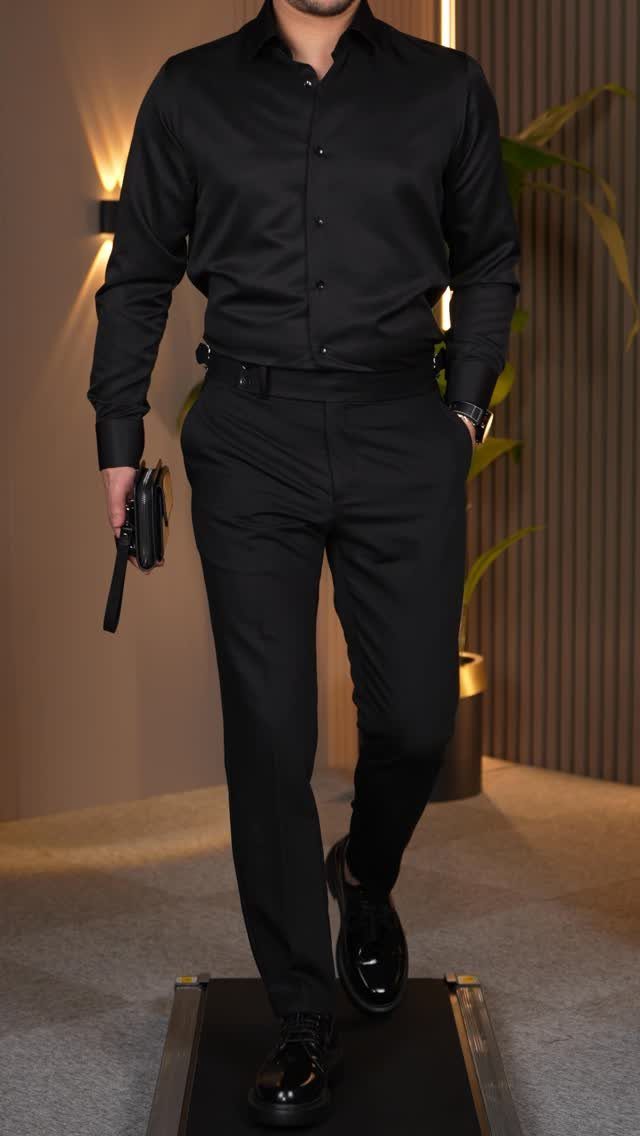 Man in an all-black formal casual outfit walking on a treadmill.