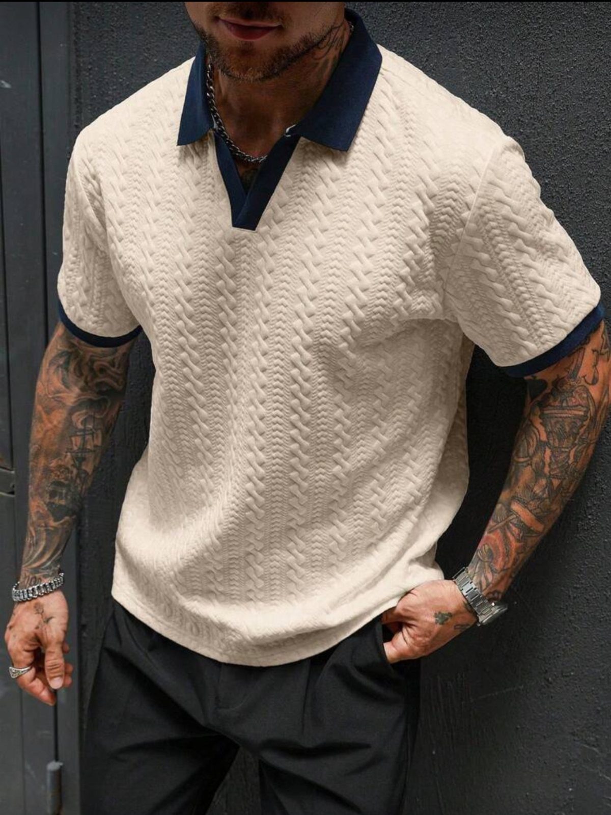 Man wearing a cream textured knit polo shirt with navy trim and black trousers.