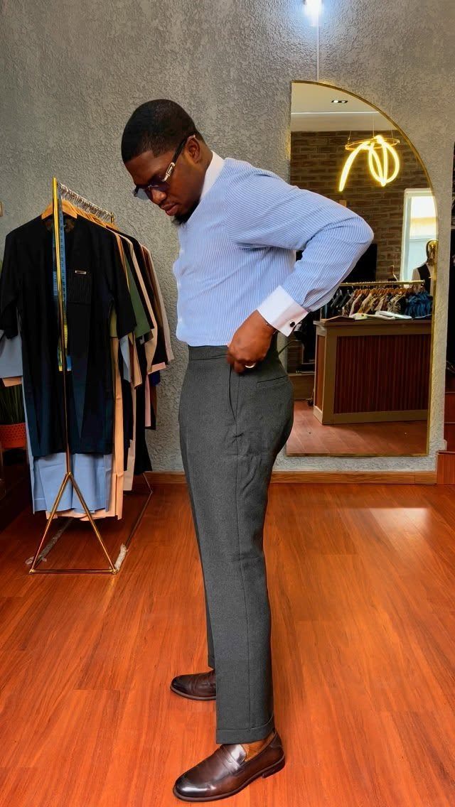 A man in a blue shirt and grey trousers posing in a clothing store.