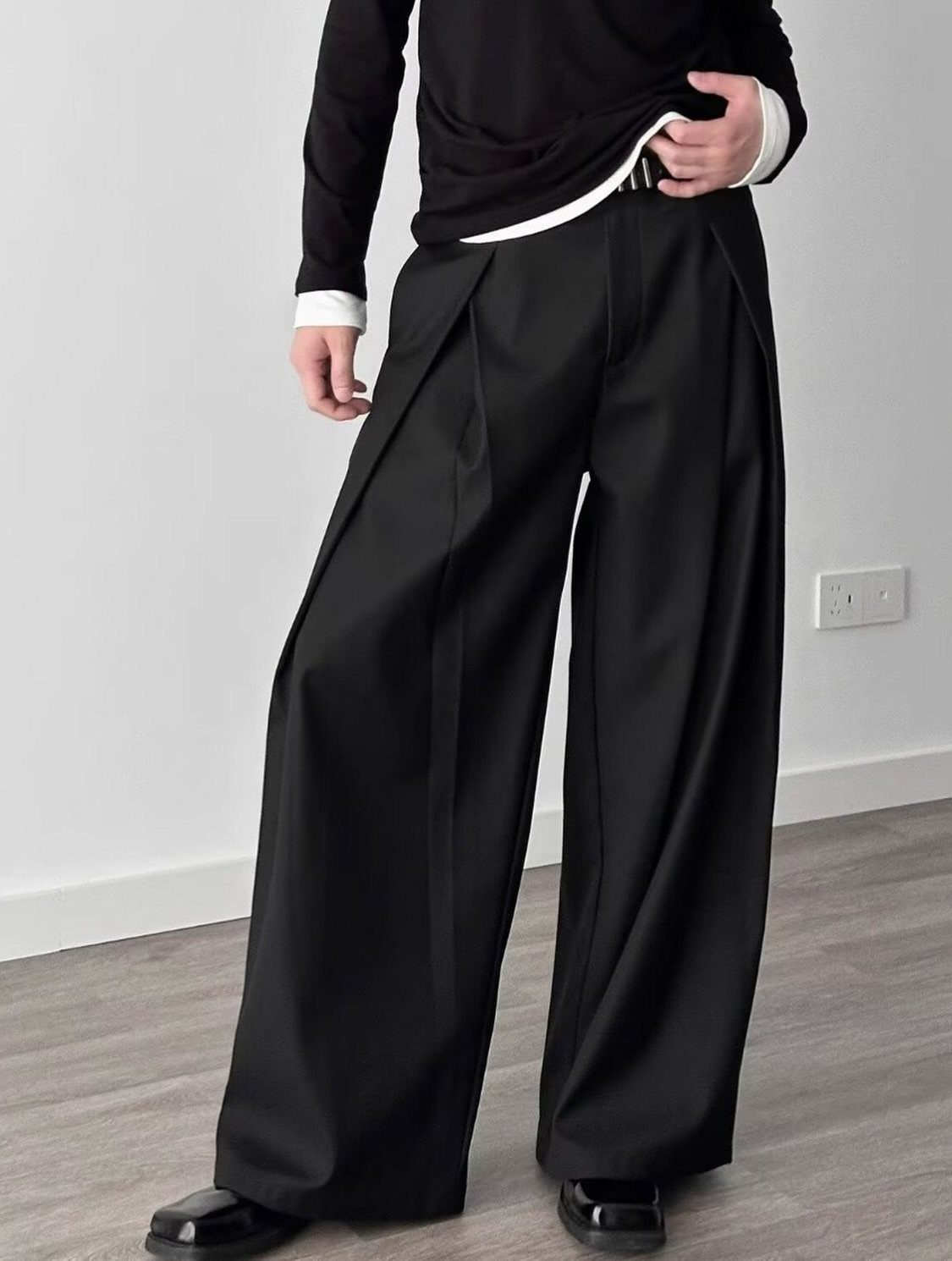 Person wearing black pleated wide-leg trousers and a black long-sleeve shirt.