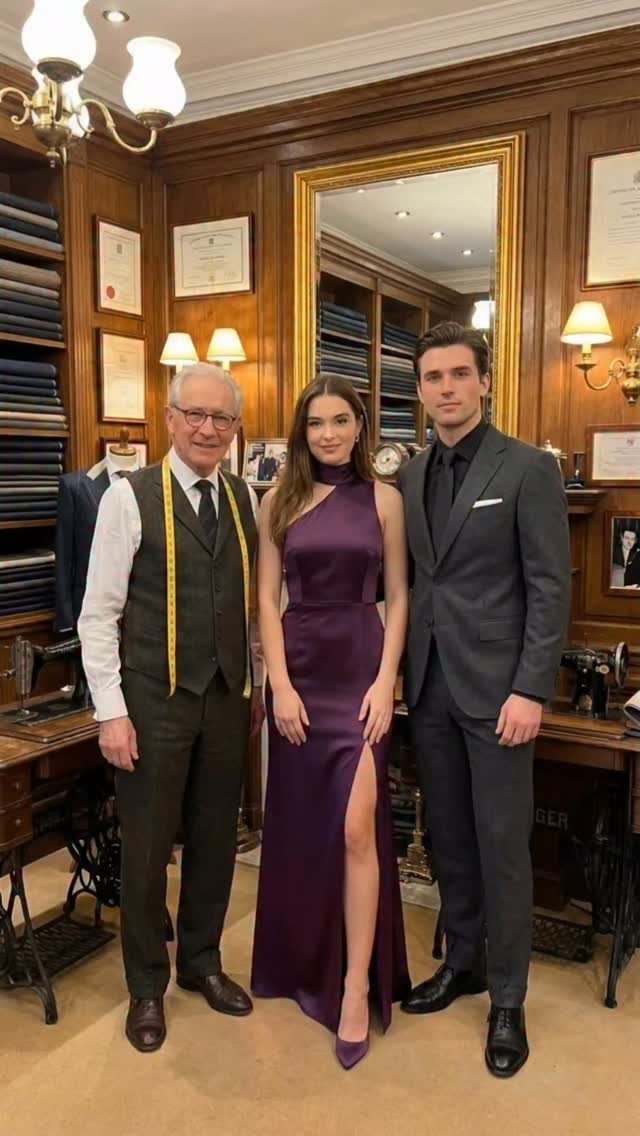 Three people dressed in formal attire posing inside a classic wood-paneled tailor shop.